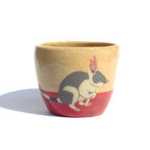 Load image into Gallery viewer, A handmade ceramic cup in a light coloured speckled clay with a hand drawn illustration of a bilby and a red colour along the bottom like the desert sand.