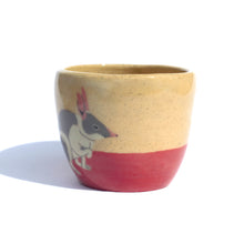 Load image into Gallery viewer, A handmade ceramic cup in a light coloured speckled clay with a hand drawn illustration of a bilby and a red colour along the bottom like the desert sand.
