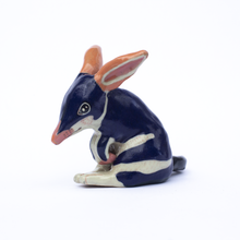 Load image into Gallery viewer, Left side view of a handmade ceramic sculpture of a dark blue and white bilby with pink ears and nose.