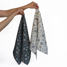 Load image into Gallery viewer, Two arms stretched out with each hand holding a tea towel, one green and one white with a repeat pattern of faces of an orangutan, proboscis monkey, gibbon, silver leaf monkey and her orange baby, a macaque and some green leaves.