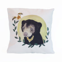 Load image into Gallery viewer, Organic cotton cushion cover with an original watercolour and hand stitched illustration of a sun bear cub, a pale yellow circle sun behind the bear, leaves framing the image with a yellow flower at the end and two bees.