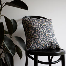 Load image into Gallery viewer, Organic cotton cushion cover with a repeat pattern of faces of an orangutan, proboscis monkey, gibbon, silver leaf monkey and her orange baby, a macaque and some green leaves on a forest green background. The cushion is sitting on a chair with some leaves to the left of the image.