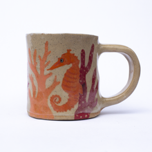 Load image into Gallery viewer, Handmade ceramic mug with illustrations of a seahorse and coral in orange and red colours.