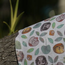 Load image into Gallery viewer, The white 'Primate' organic cotton tea towel with a repeat pattern of faces of an orangutan, proboscis monkey, gibbon, silver leaf monkey and her orange baby, a macaque and some green leaves.
