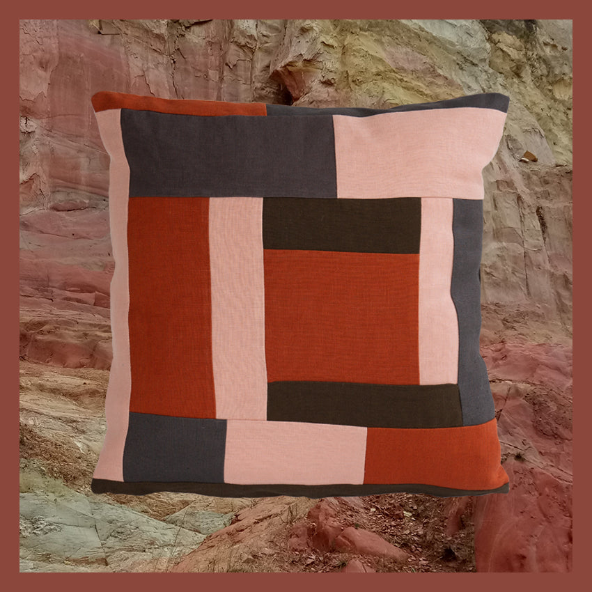 Nyattski one-of-a-kind and zero waste patchwork cushion with grey, blush pink, burnt orange, and dark olive green colours photoshopped on a photograph of pink, white and yellow-toned clay at Black Hill Lookout and an earthy coloured pink border.