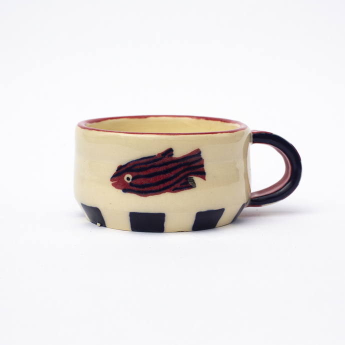 Handmade ceramic mug with a red rim, blue squares at the base, blue and red handle and an illustration of  a red and blue striped fish.