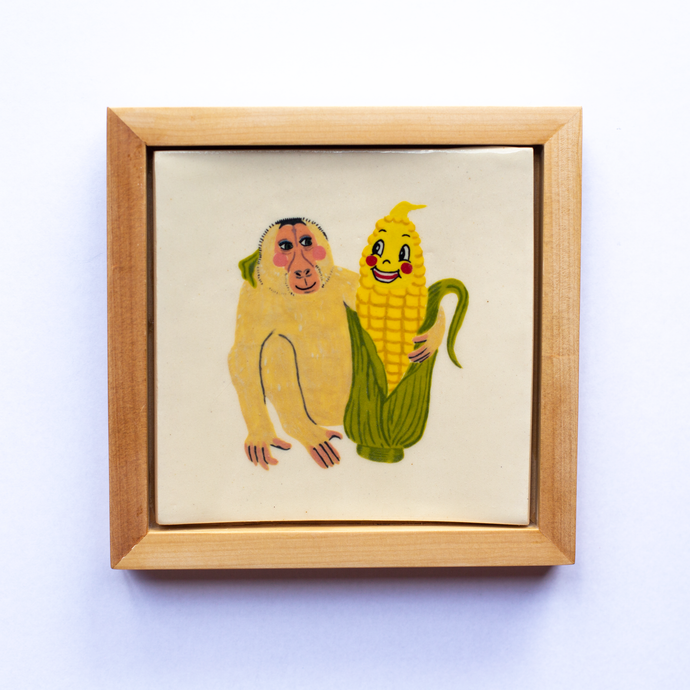 Framed ceramic art tile with an illustration of a monkey and anthropomorphic  corn looking at each other, and with their arms around one another.