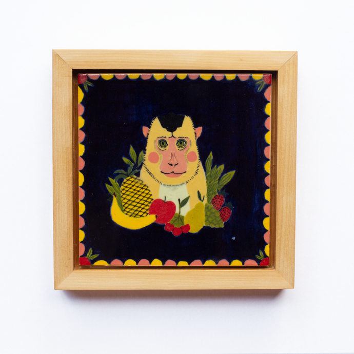 Framed ceramic art tile with a colourful illustration of a monkey sitting between some fruit, a deep blue background, and a scalloped border.