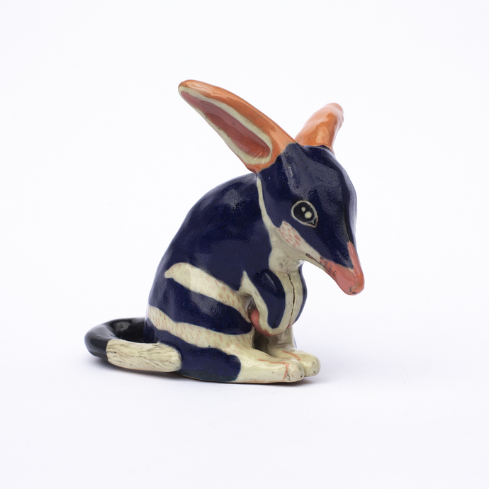 Right side view of a handmade ceramic sculpture of a dark blue and white bilby with pink ears and nose.