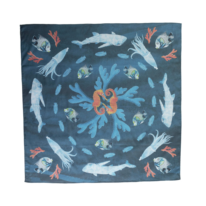 A square scarf in a blue colour with sea creatures making a circular pattern like they are synchronised swimming. Orange seahorses, blue and white squids, whale sharks, fish with a little bit of yellow, and blue and orange coral. 