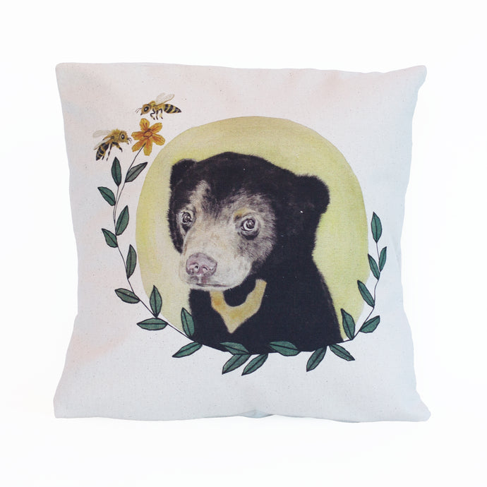 Organic cotton cushion cover with an original watercolour and hand stitched illustration of a sun bear cub, a pale yellow circle sun behind the bear, leaves framing the image with a yellow flower at the end and two bees.