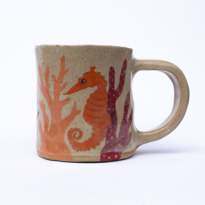 Handmade ceramic mug with illustrations of a seahorse and coral in orange and red colours.