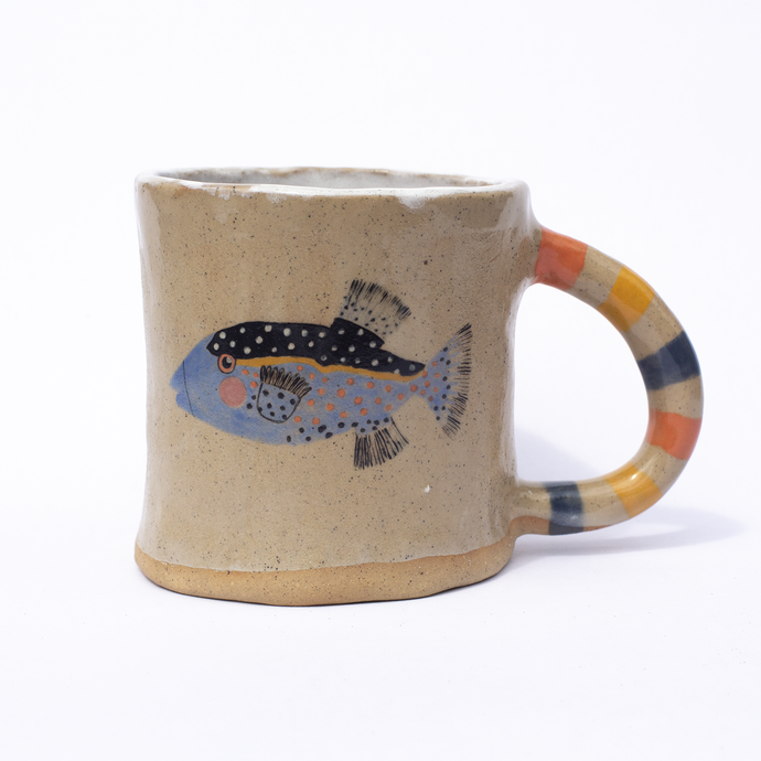 A handmade ceramic mug with a striped handle and an illustration of a spotty fish.