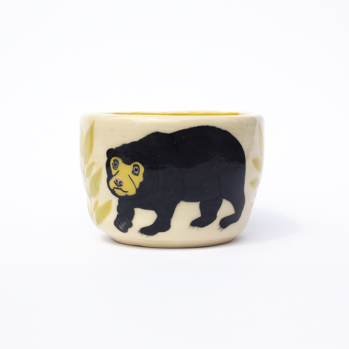 Handmade  ceramic cup with an illustration  of a sun bear and some leaves.