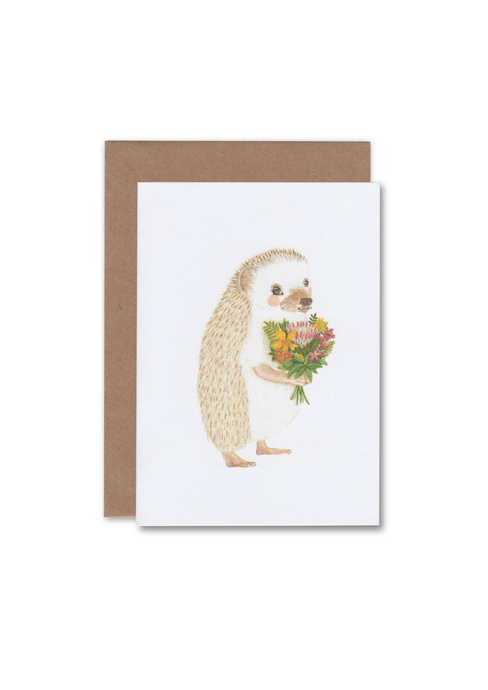 A greeting card lying flat on an envelope with an illustration of a hedgehog holding a bunch of flowers.