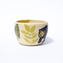 Load image into Gallery viewer, Side view of handmade ceramic cup with an illustration of leaves and a sun bear.
